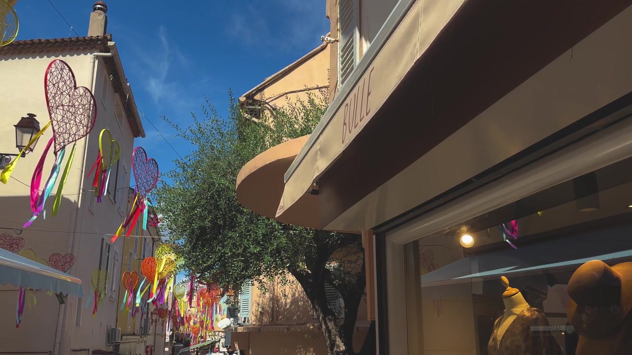 Cuori e nastri intrecciati vivaci decorano una stretta strada mediterranea fiancheggiata da boutique, edifici color pastello e architettura tradizionale