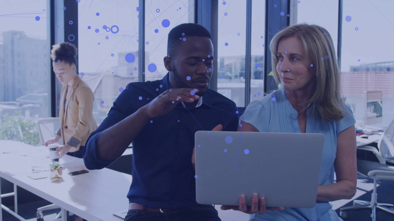 Business team working on laptop by windows, man gesturing causing blue circles overlaying laptop