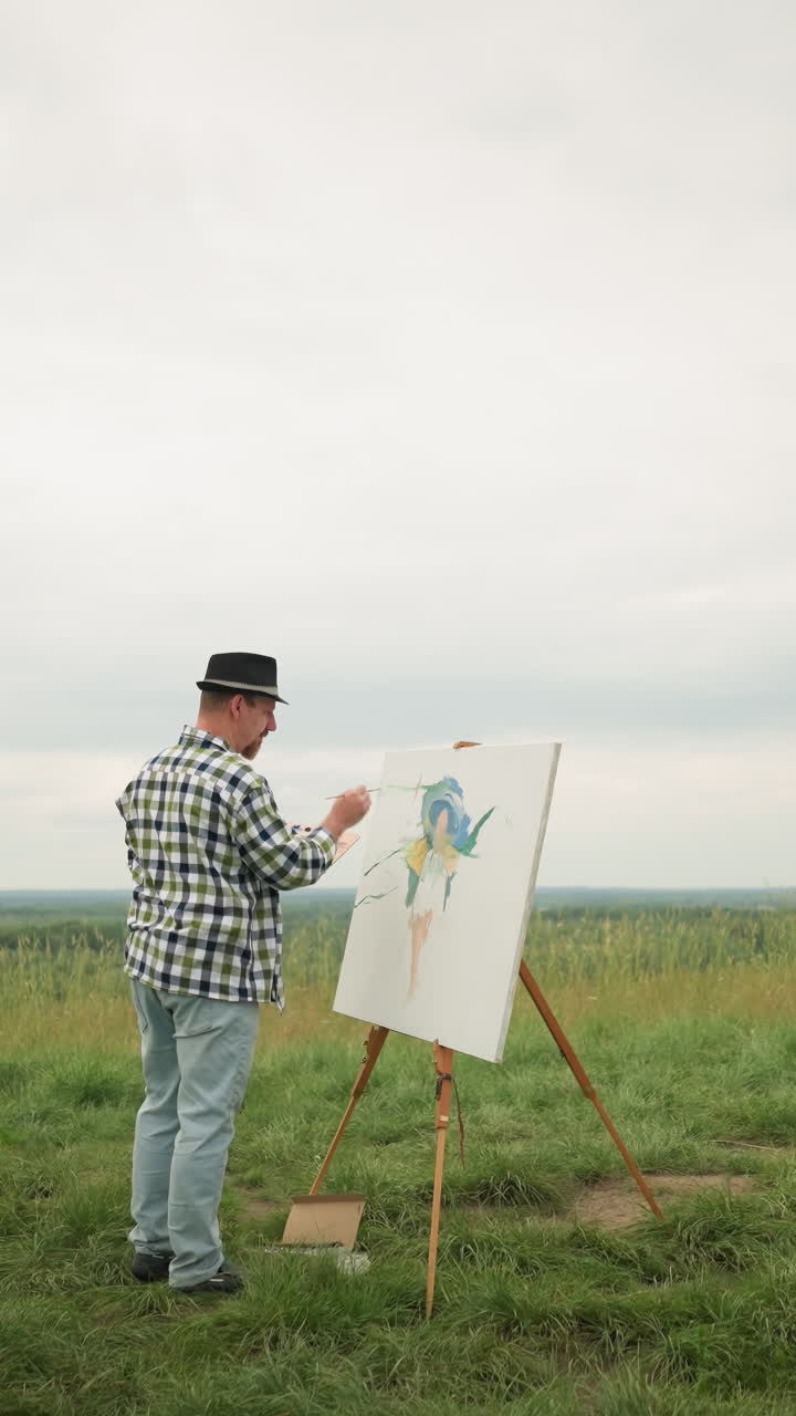 A painter wearing a hat, checkered shirt, and jeans is deeply focused on creating a masterpiece on a canvas, set in the middle of a lush grassy field beside a lake under a cloudy sky