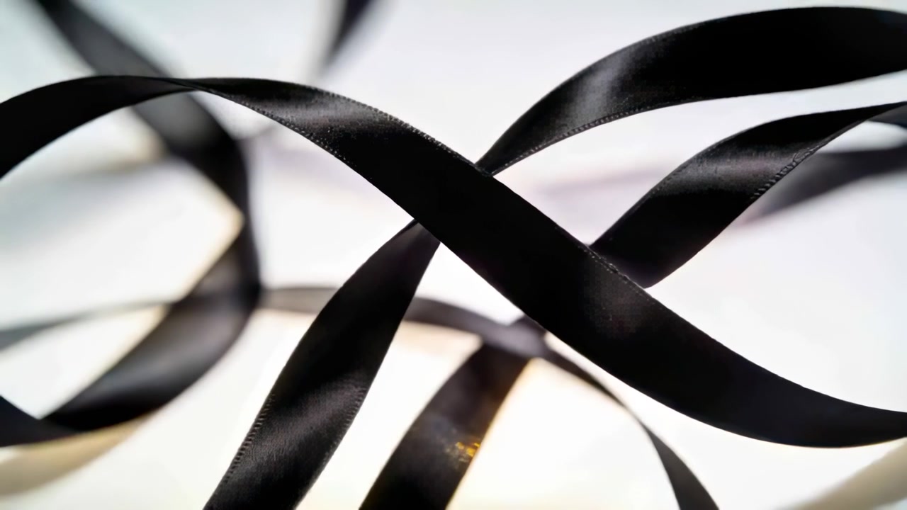 Drifting black satin ribbons shifting right after soft breeze across studio backdrop with backlight