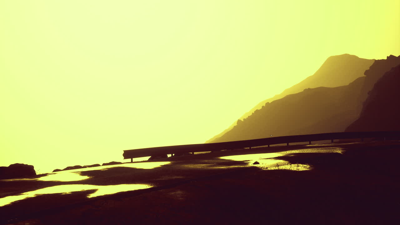 Golden sunset casts warm light on mountain silhouette and winding road