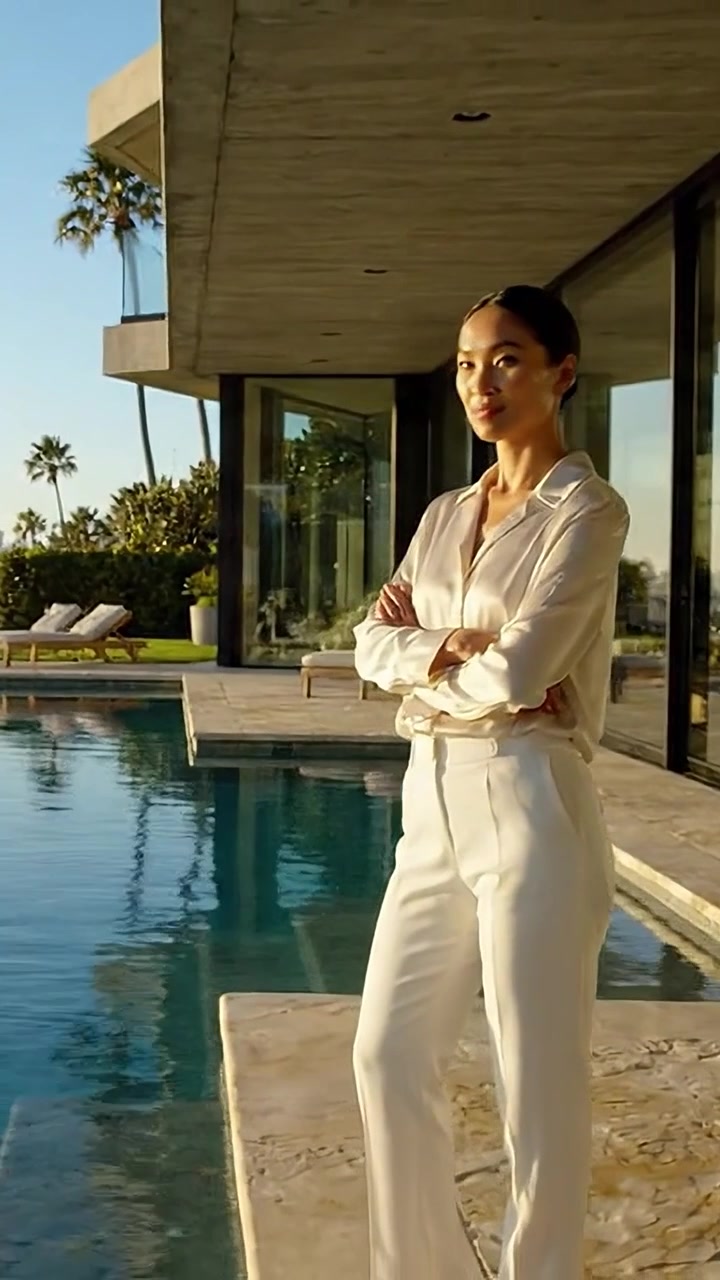 Reflejo elegante: Un individuo sofisticado posa con gracia junto a una lujosa piscina a la hora dorada, capturando calma en medio de la belleza arquitectónica moderna.