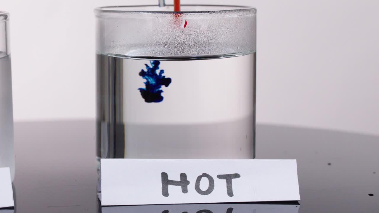 Blue and yellow dye disperses rapidly in hot water glass under bright, even studio lighting
