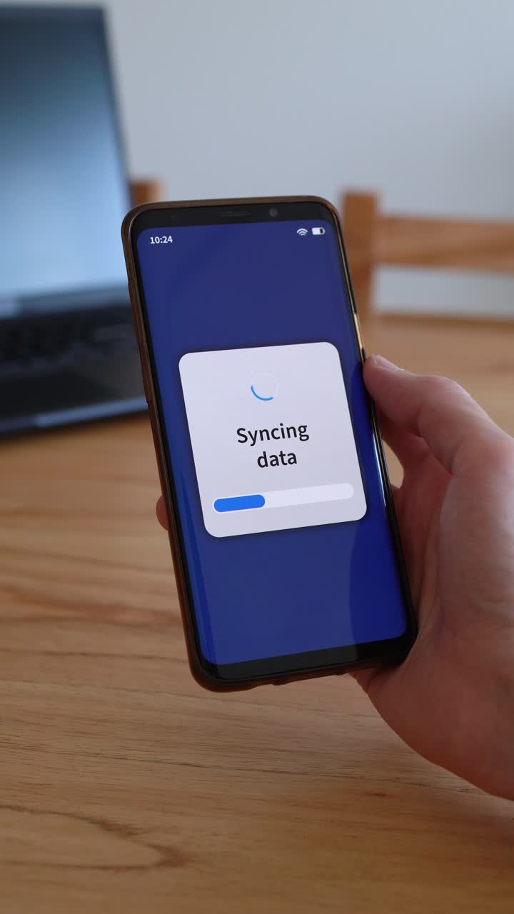Vertical shot of smartphone syncing data with cloud storage. Laptop on the background