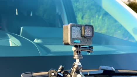 A stationary action camera is mounted on a car windshield in bright daylight, capturing the scenic surroundings of Queenstown, New Zealand