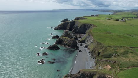 Drone-Volando-Hacia-El-Oeste-A-Lo-Largo-De-La-Costa-De-Cobre-Waterford-Irlanda-Sobre-Las-Pilas-De-Mar-Que-Bordean-La-Costa-En-Un-Cálido-Día-De-Julio