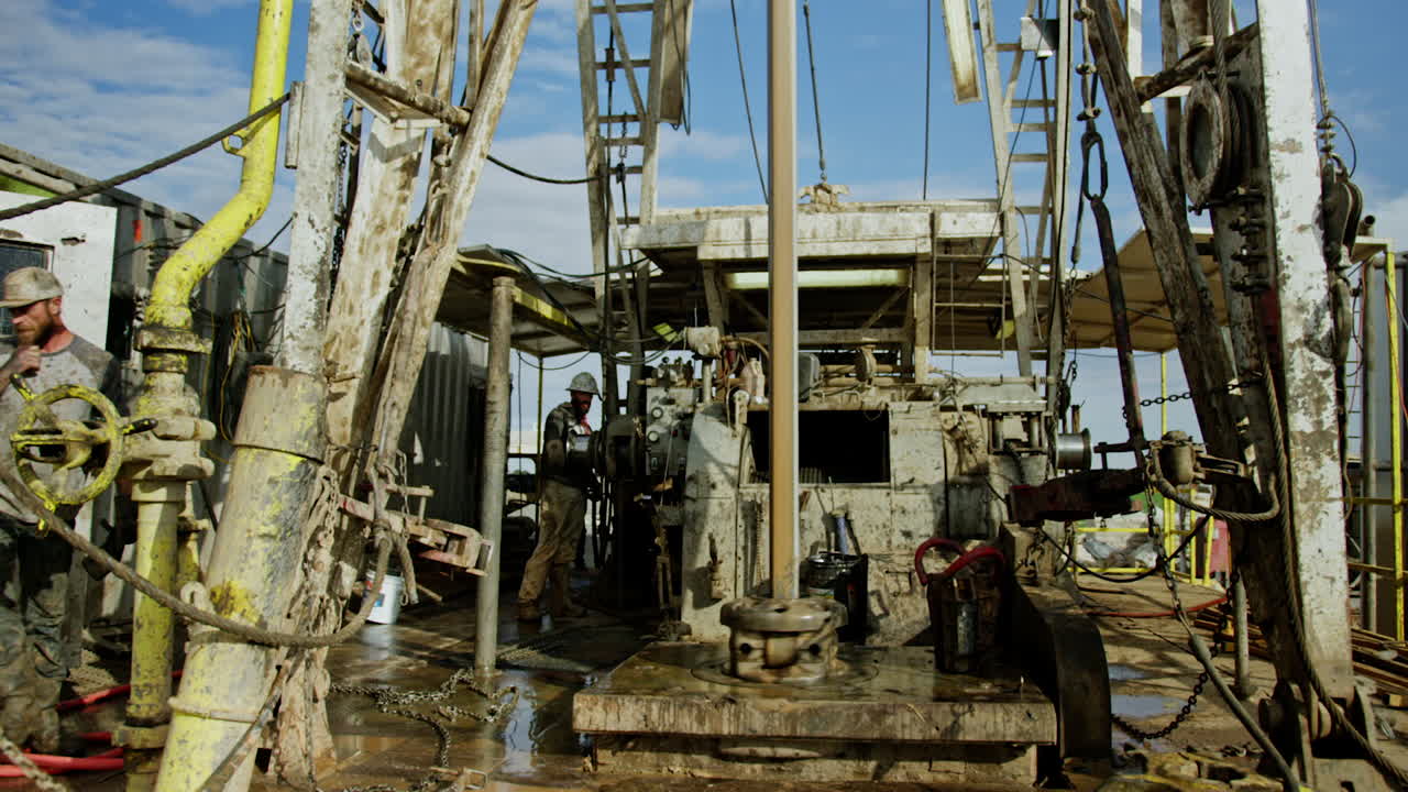 Men work at the rig for oil production. Equipment is operating to drill the natural resources.