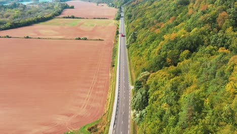 There-is-a-road-in-the-middle-of-the-shot,-on-one-side-of-the-road-is-a-big-forest,-on-the-other-side-there-is-brown-ground