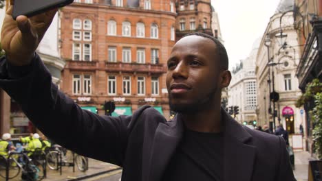 Male-taking-a-photo-on-his-smart-phone-on-a-street-in-London-City