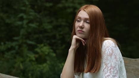 summer portrait of a beautiful red-haired girl sitting in the park and bored