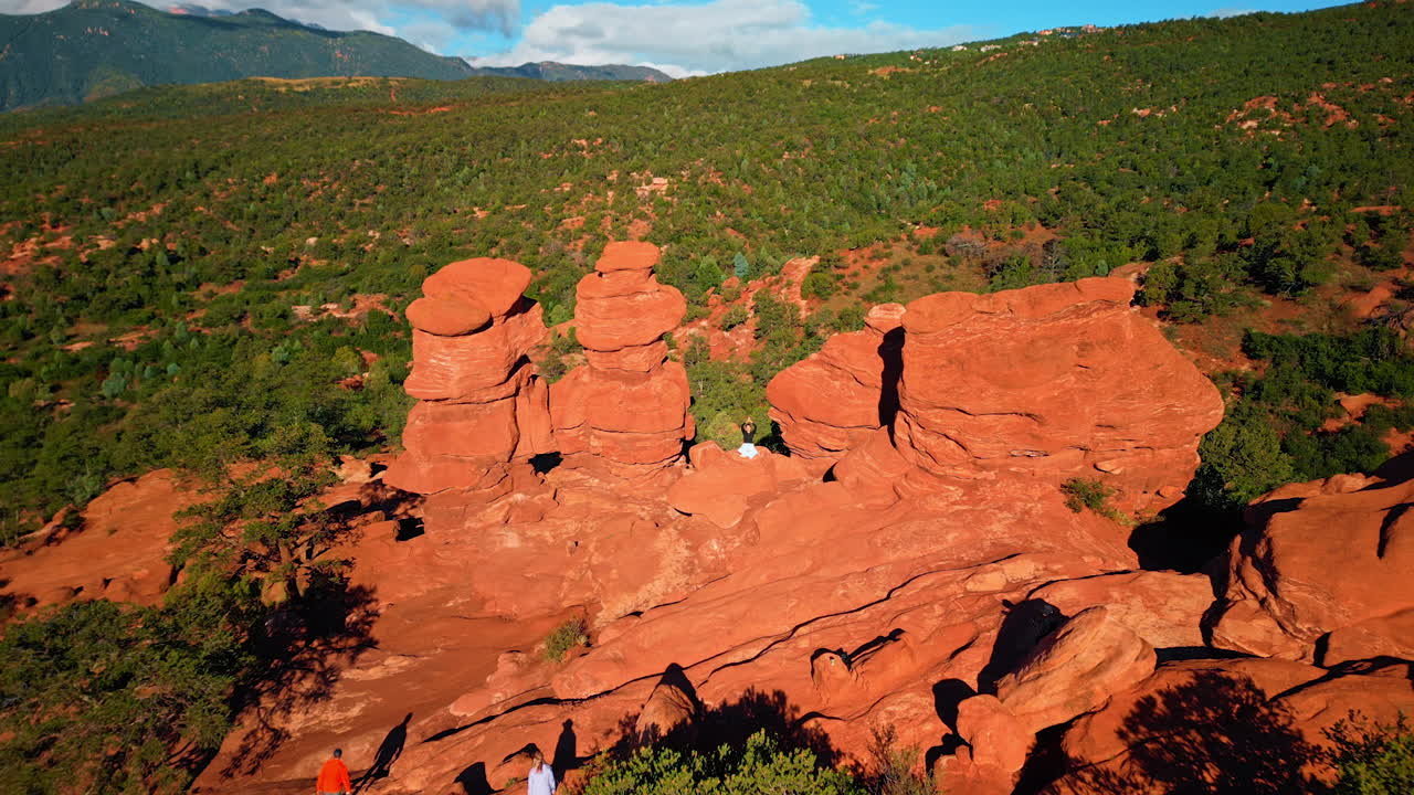 Distancing from a woman sitting in lotus pose with her hands folded above head on the red rocks. Drone rising high over Bentonite Hills, Utah, USA