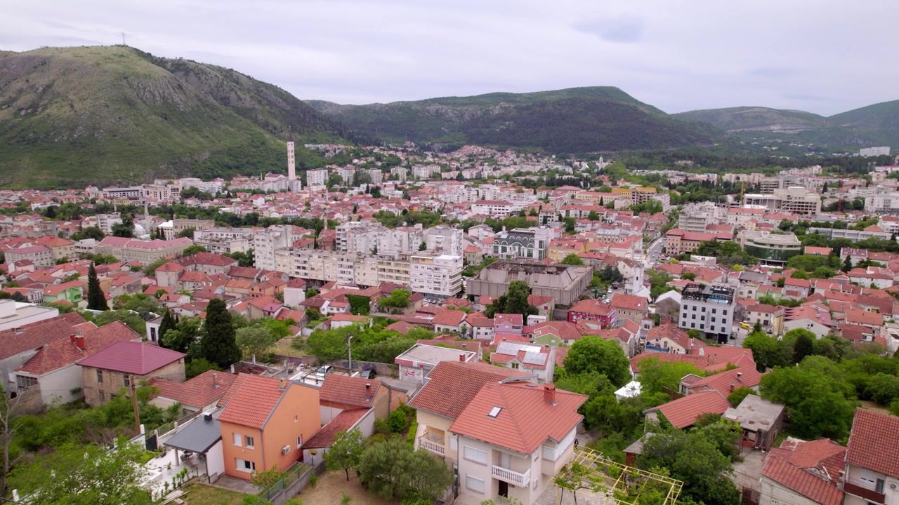 Bulutlu gökyüzünün altında, kırmızı çatılı evleri ve çevresindeki dağlarla Mostar merkezinin drone ile havadan genel çekimi, Bosna Hersek.