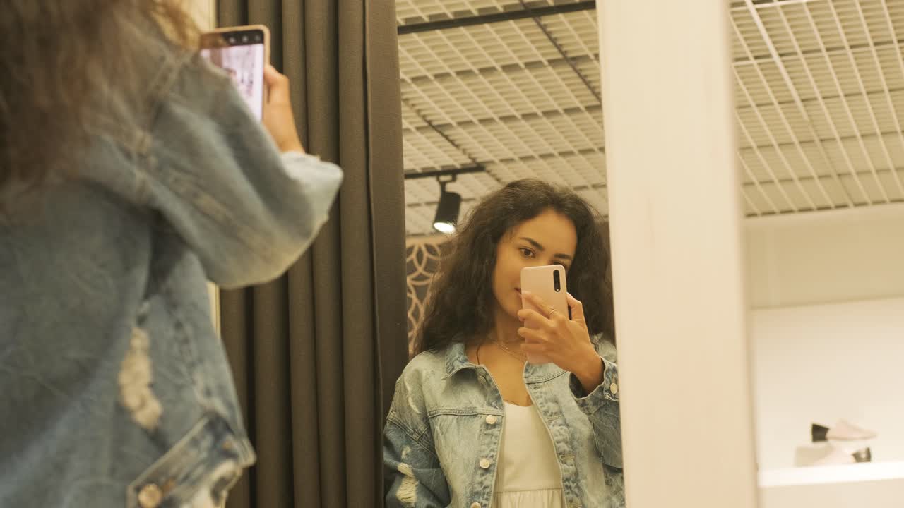 Una giovane ragazza si veste vicino a uno specchio. Sceglie un vestito per le vacanze e si fa un selfie.
