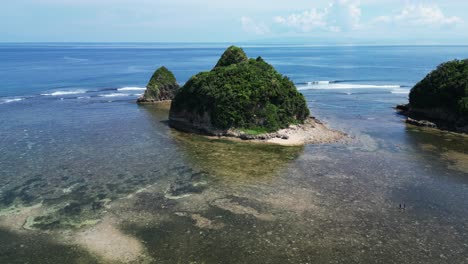 Orbiting-aerial-view-of-tropical-islet-in-stunning-ocean-cove-with-clear-turquoise-waters-and-crashing-waves