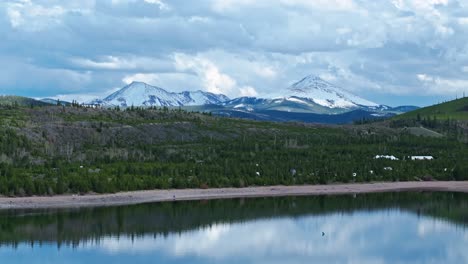 Drone-rises-above-Dillon-Reservoir-to-reveal-evergreen-forest-and-snowcapped-peaks-of-Frisco-Colorado