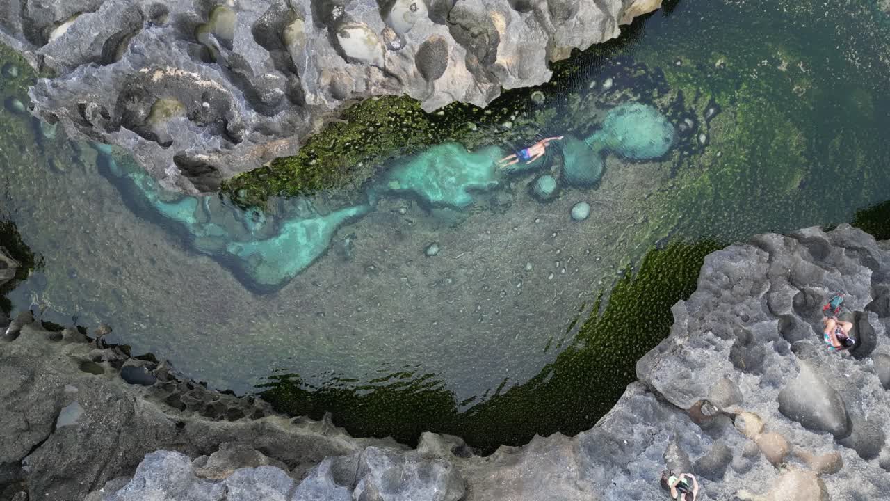 Crystal clear water, man swims in lagoon billabong by eroded rock