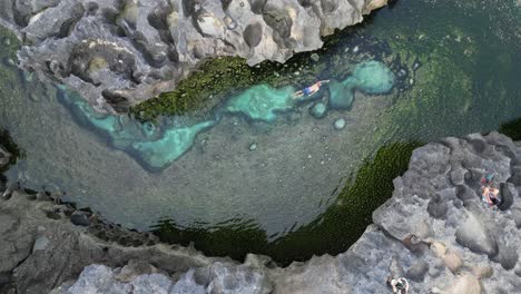 crystal clear water, man swims in lagoon billabong by eroded rock