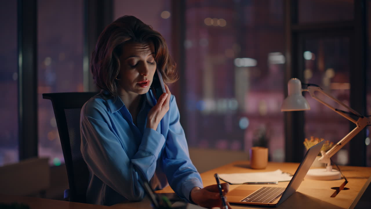 Tired professional talking mobile phone at night office writing notebook closeup