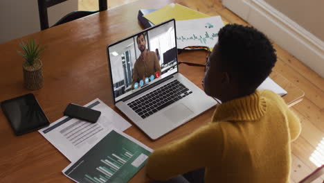 african american businesswoman sitting at desk using laptop having video call with colleague