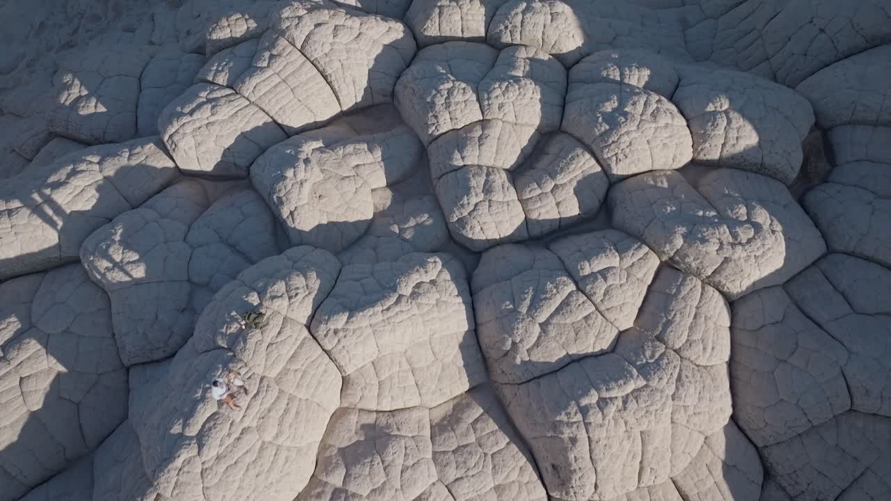 A top-down drone shot revealing the unique sandstone rock features of White Pocket Arizona surrounded by sandy desert and blue skies at sunset