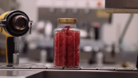 close-up tracking of clear bottle with red multivitamin supplements on conveyor