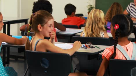 Schoolgirl-whispering-into-her-friends-ear-in-classroom