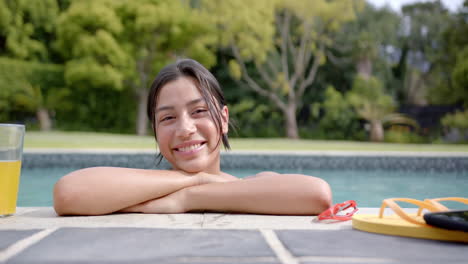 Retrato-De-Una-Adolescente-Birracial-Feliz-Parada-En-Una-Piscina-Soleada,-Cámara-Lenta