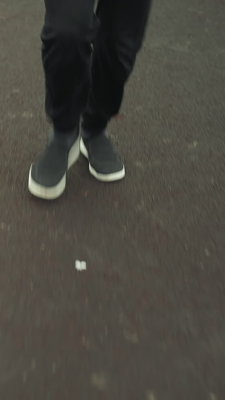 Close up leg view of two individuals wearing joggers and sneakers, walking on a track near a grassy field before transitioning into a jogging pace