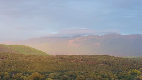 drone flight over a valley filmed in 70mm. a sunlit area stands out dramatically as rays break through the clouds, highlighting the forest as if revealing a mystical apparition.