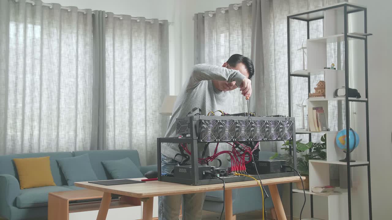 안경을 쓴 아시아인 남자가 암호화폐 채굴을 위한 채굴 기계를 고치고 있습니다.