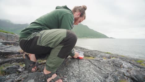 excursionista masculino preparando su caña de pescar junto al lago de la montaña segla en la isla senja, noruega