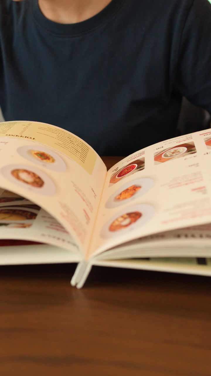 Person bladrer gennem detaljeret menu, peger på retter, naturlig belysning, stabilt mellembillede, afslappet spisning