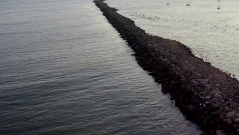 long rock jetty in the ocean with boats and birds