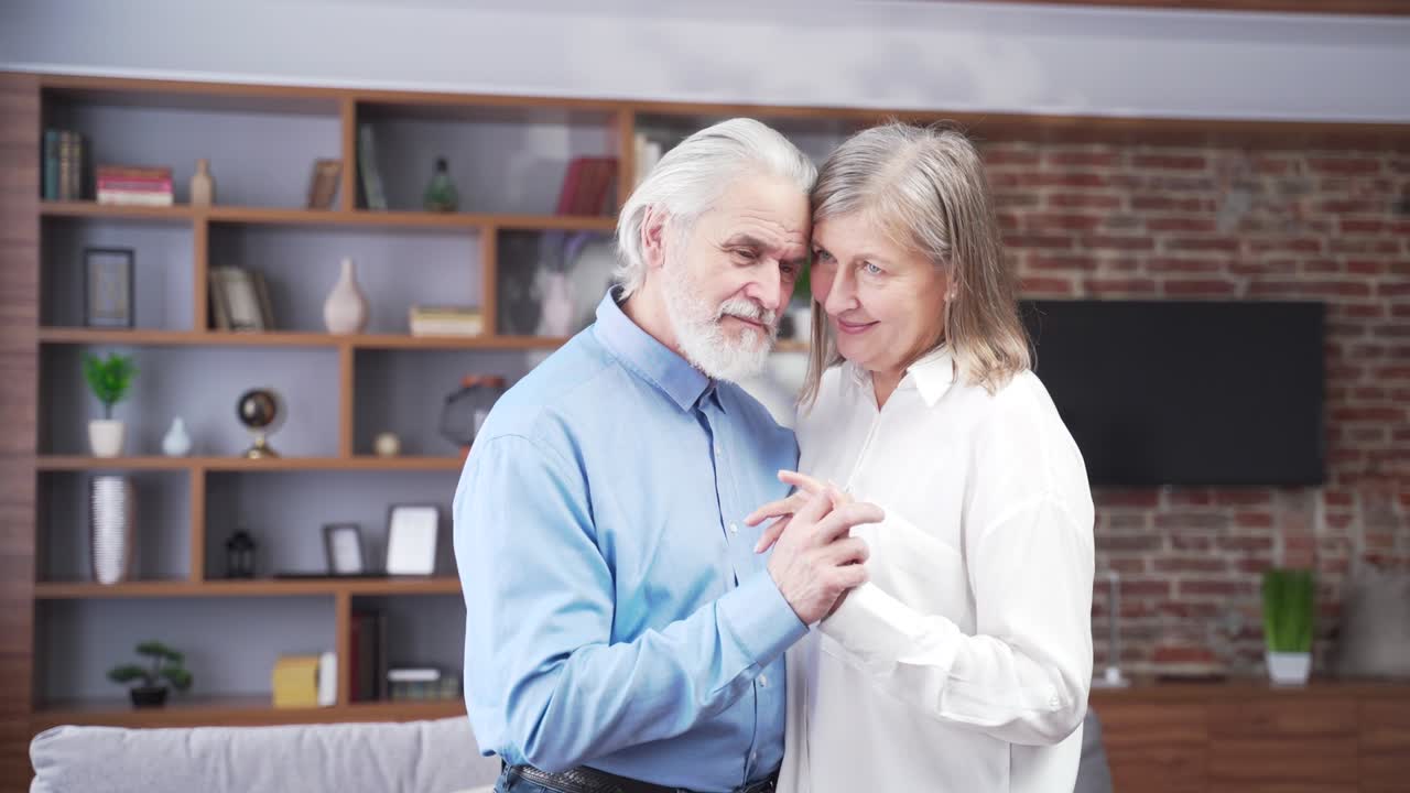 senior elderly romantic couple in love dancing at home. Old gray haired family hug together. Husband and wife celebrate wedding anniversary while listen to music