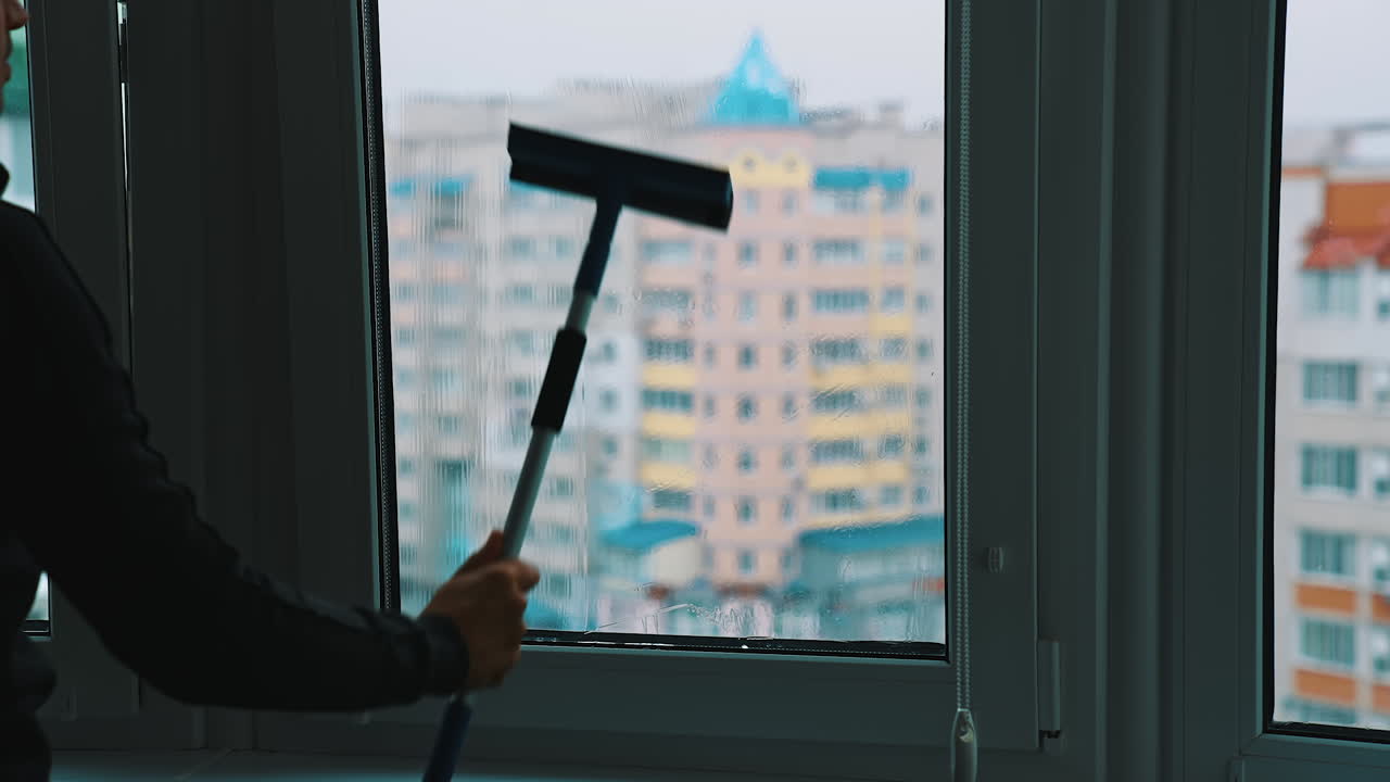 Worker washing plastic window. Man cleaning window with a brush inside the high building in the city. Washing glass window.