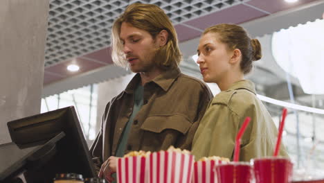 happy couple selecting movie from screen and buying tickets at cinema 1