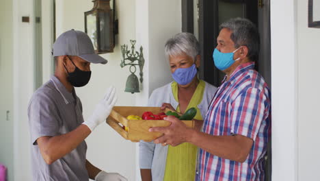 una pareja biracial y un repartidor de comida en la puerta con máscaras faciales.