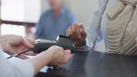 mujer biracial pagando con tarjeta de crédito en la recepción de una clínica dental moderna