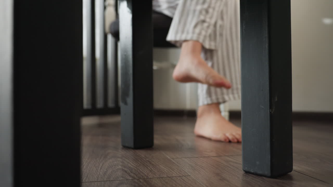 Youth feet in striped pyjamas step past bed on wooden floor, soft rug ahead, curtain dividing room from sitting room, morning calm, smooth movement, bedroom decor, low angle leg view in natural light