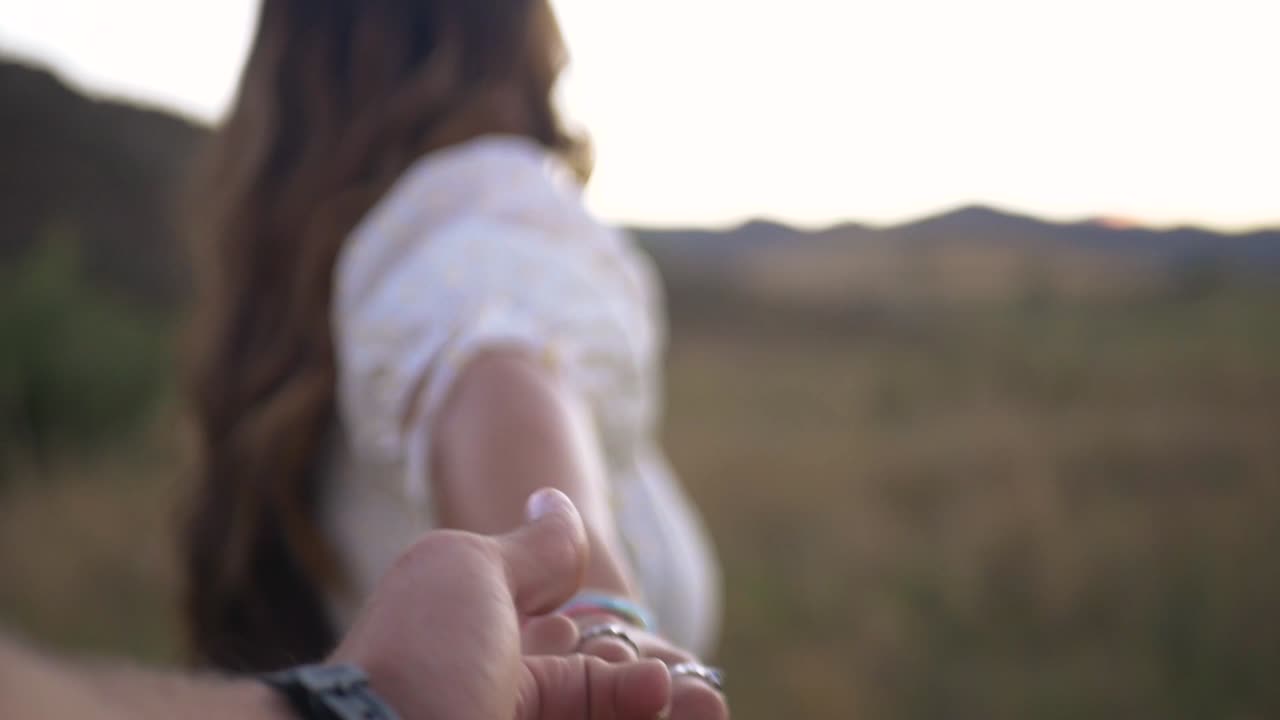 Girl and guy hold hands as girl drags guy through a field during sunset