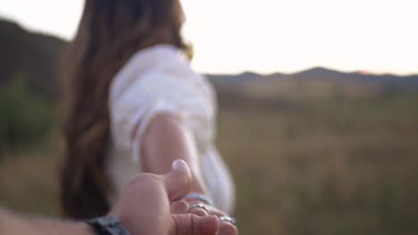 girl and guy hold hands as girl drags guy through a field during sunset