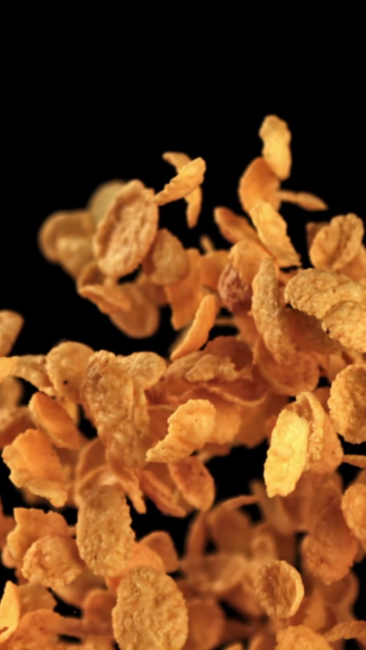 Cornflakes dorati che cadono e risalgono al rallentatore su sfondo nero