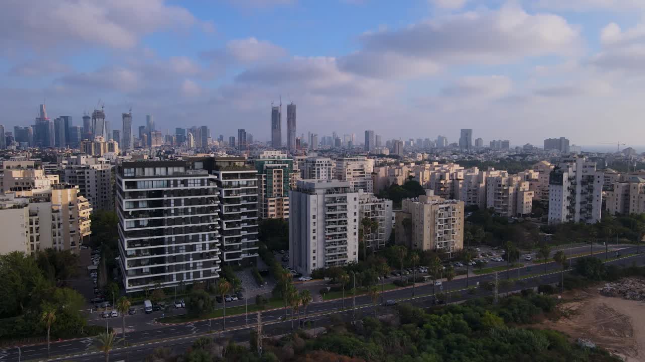 Drone shot over a street in Tel Aviv showing a residential building visibly damaged after a recent strike, with modern city skyscrapers in the background.
