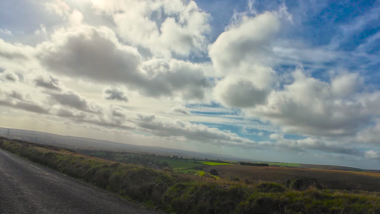 Smooth Tracking Shot Along Rural Countryside Road with Large Open Landscape with Cloudy Bright Sky with Fields. Natural British Landscape Over Wales, UK