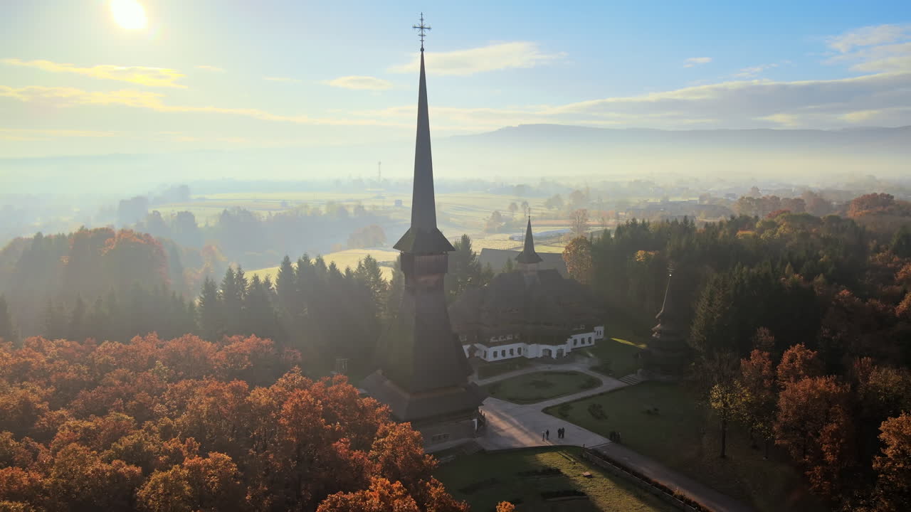 Aerial drone view of the Peri-Sapanta Monastery at sunrise, Romania. Main church and a building, visitors, yellowing forest around