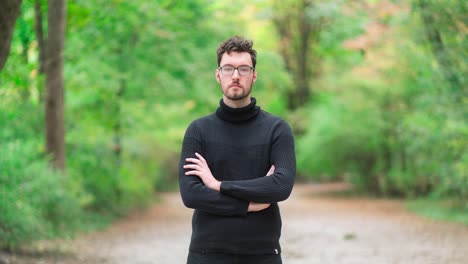 time lapse of a young caucasian man with a beard and glasses, dressed in a turtleneck sweater standing in an autumnal park, while passersby, people, and cyclists move and scurry around him