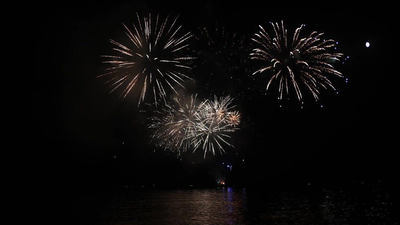 Colorful fireworks bursting in a dark night sky, illuminating the water below with vibrant reflections during a celebration