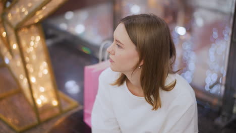 woman seated with reflective expression surrounded by festive lighting, gentle bokeh effects create a serene and dreamlike atmosphere as light reflections play softly on her thoughtful face