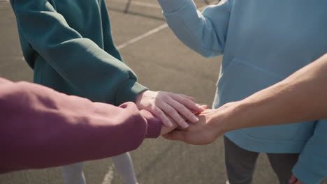 cerca de las manos de personas con capuchones que se unen como un equipo durante un juego de voleibol al aire libre, simbolizando la unidad, el trabajo en equipo y la colaboración bajo un cielo brillante en un entorno al aire libre