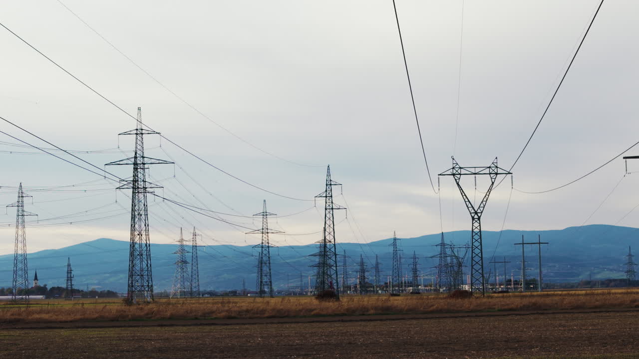High voltage transmission towers and power lines cross a rural landscape during daylight